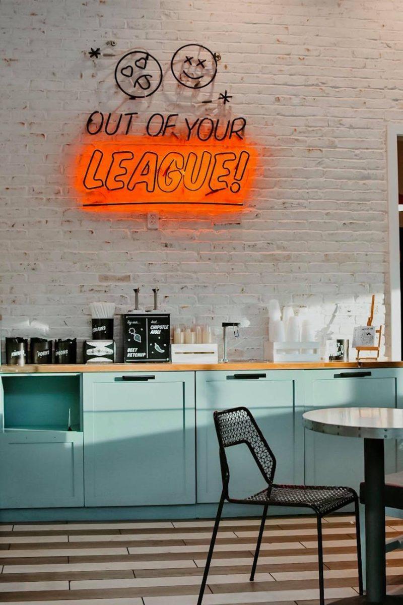 a neon signage hanging on a white painted brick wall in a cafeteria